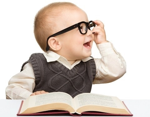 child wearing black-framed eyeglasses sitting in front of book and smiling