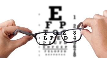 person holding eyeglasses infront of eye test letters