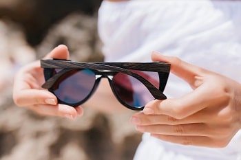 woman in white outfit holding her glasses. photo of european a woman with dark sunglasses standing outdoor
